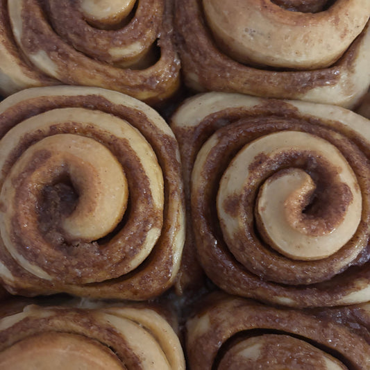 A close-up view of several cinnamon rolls arranged in a grid, showing their spiral shapes with light beige dough and dark brown cinnamon filling.